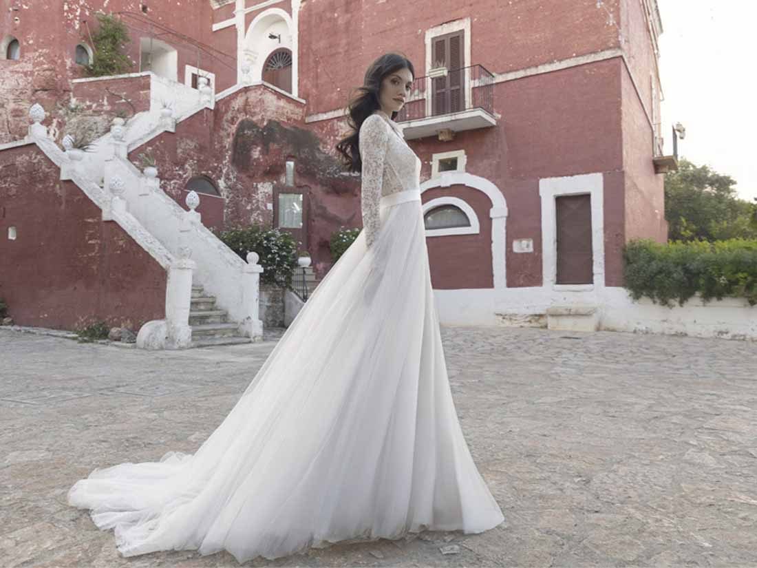 Abito da sposa Pietro De Mita in pizzo a maniche lunghe con gonna in tulle, davanti a una masseria pugliese