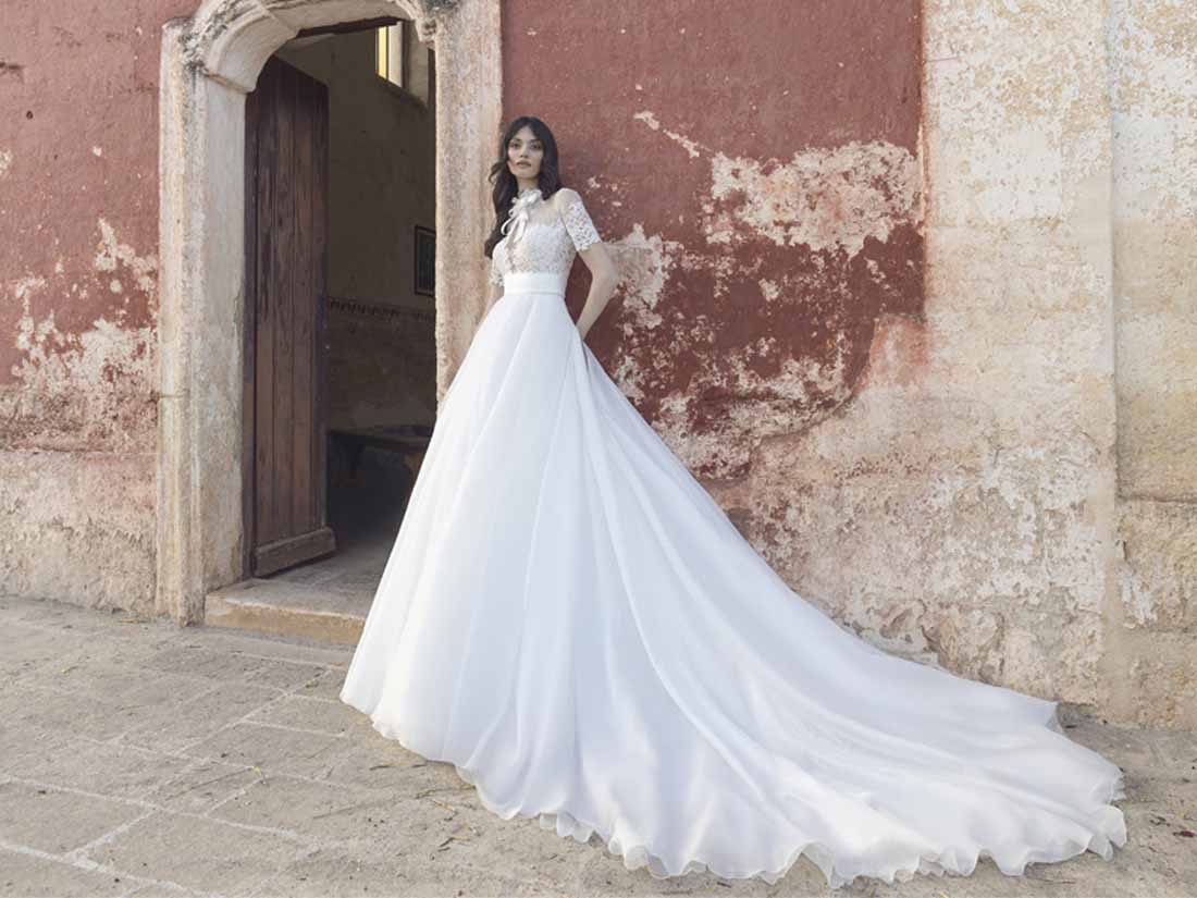 Abito da sposa Pietro De Mita a linea A con lungo strascico sulla soglia di un portale in pietra