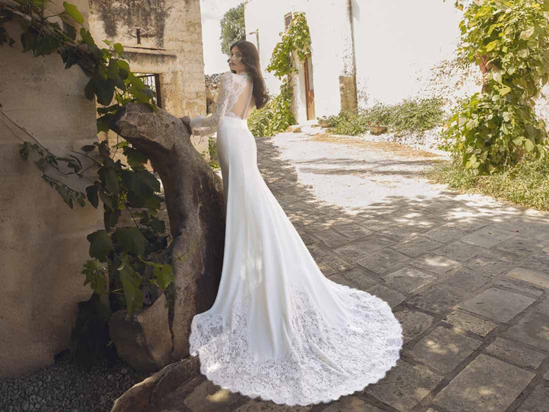 Abito da sposa Pietro De Mita con schiena scoperta e strascico in pizzo in un vicolo di pietra