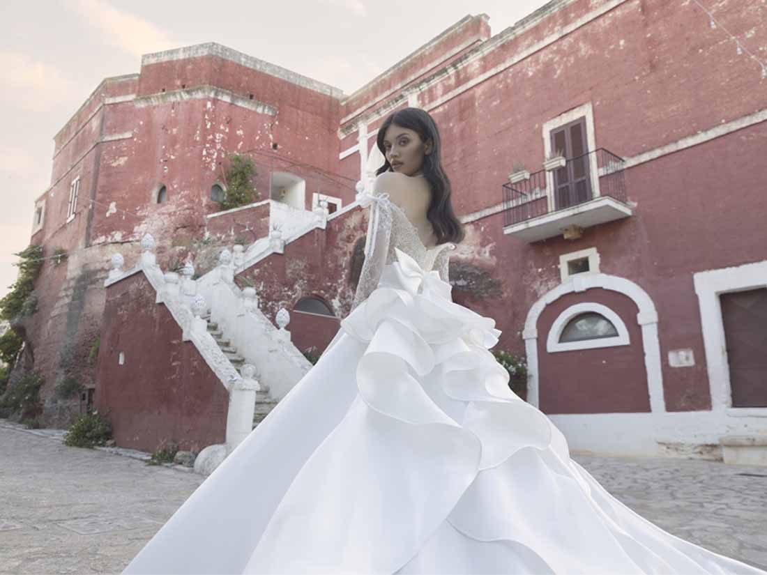 Abito da sposa Pietro De Mita con gonna a volant scultorei davanti a una masseria rossa