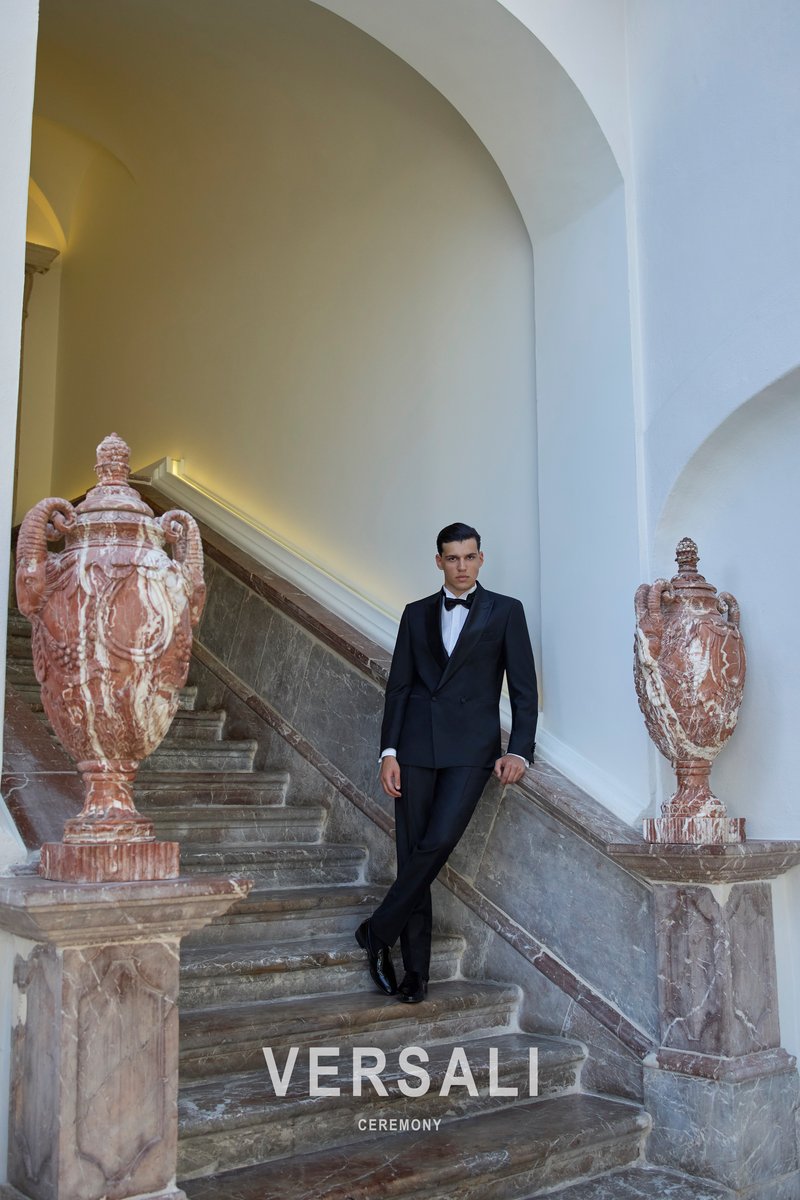 Sposo in smoking nero Andrea Versali con papillon, su uno scalone in marmo fra due anfore